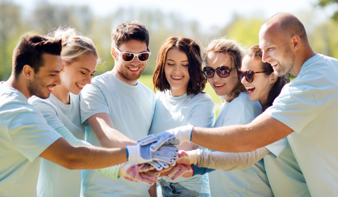 Group of happy volunteers putting hands on top in park