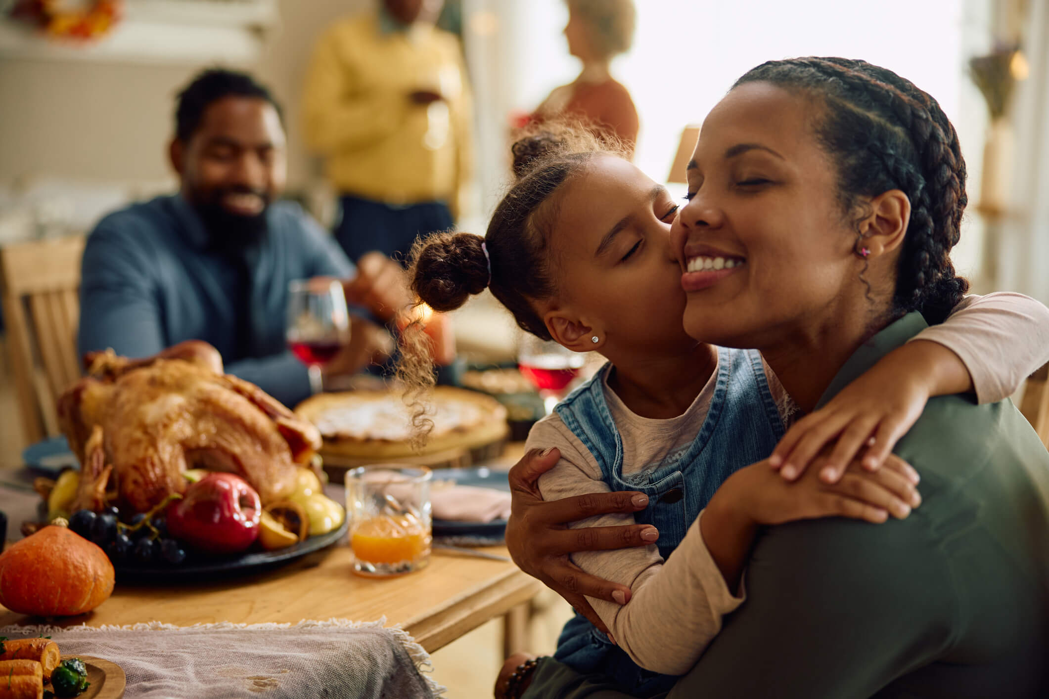 Family at holiday meal where a daughter is kissing her mother