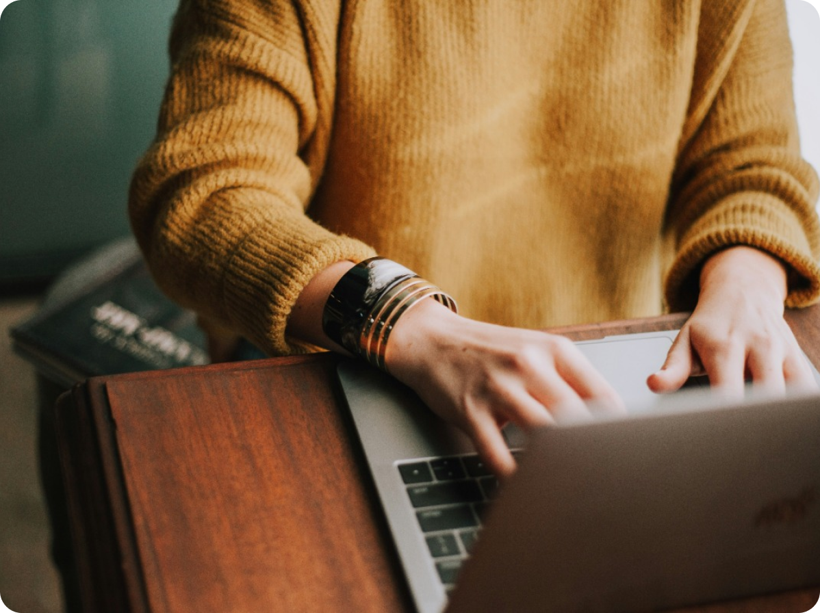 Person in a yellow sweater using a laptop computer