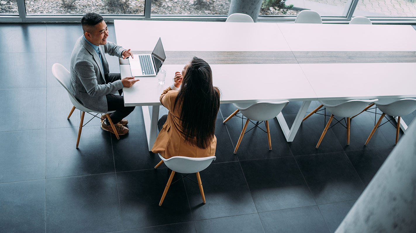 Two people seated at conference table with laptop.