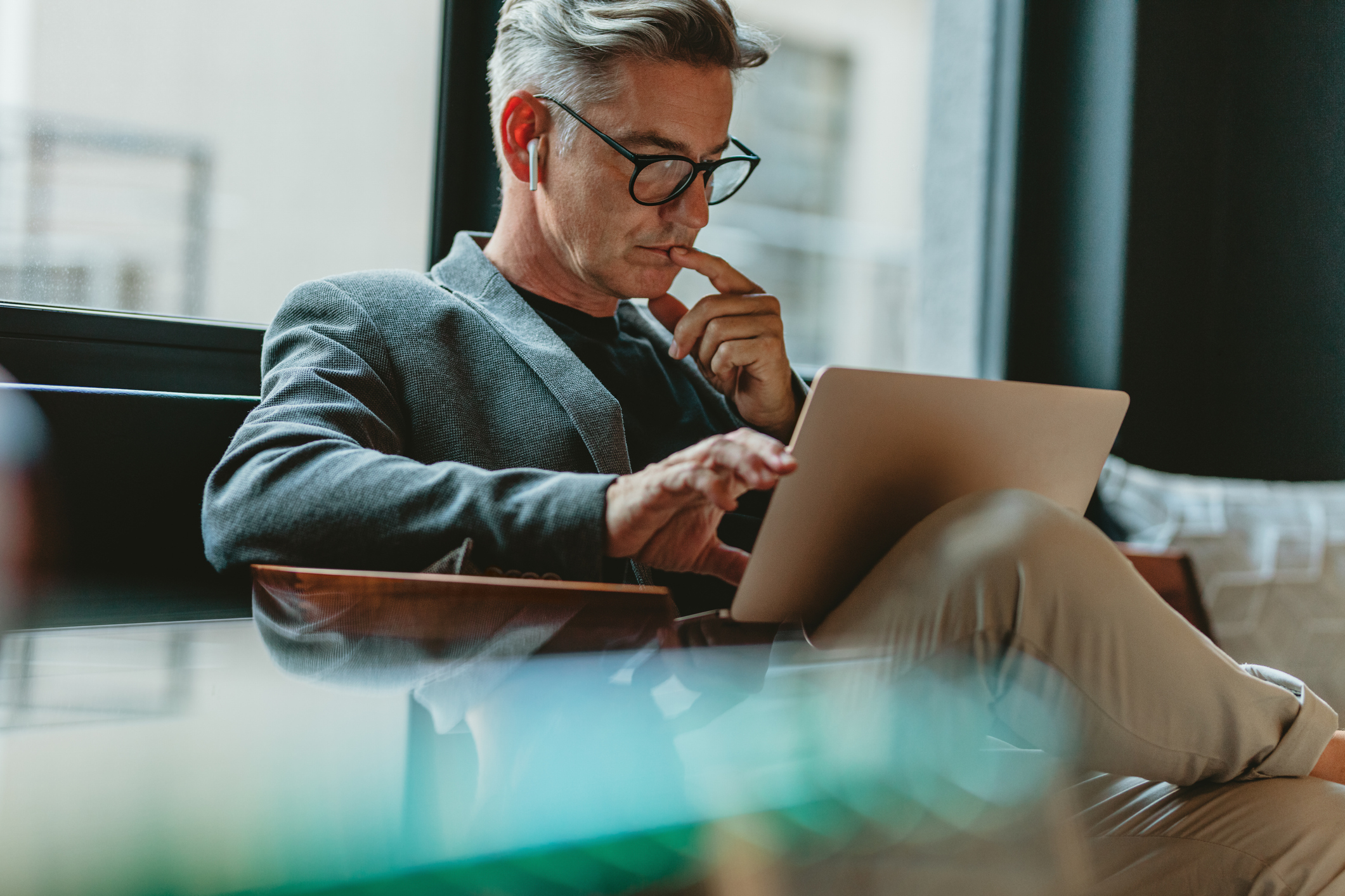 Businessman looking at laptop and thinking. Businessman reading emails on laptop in office lobby.