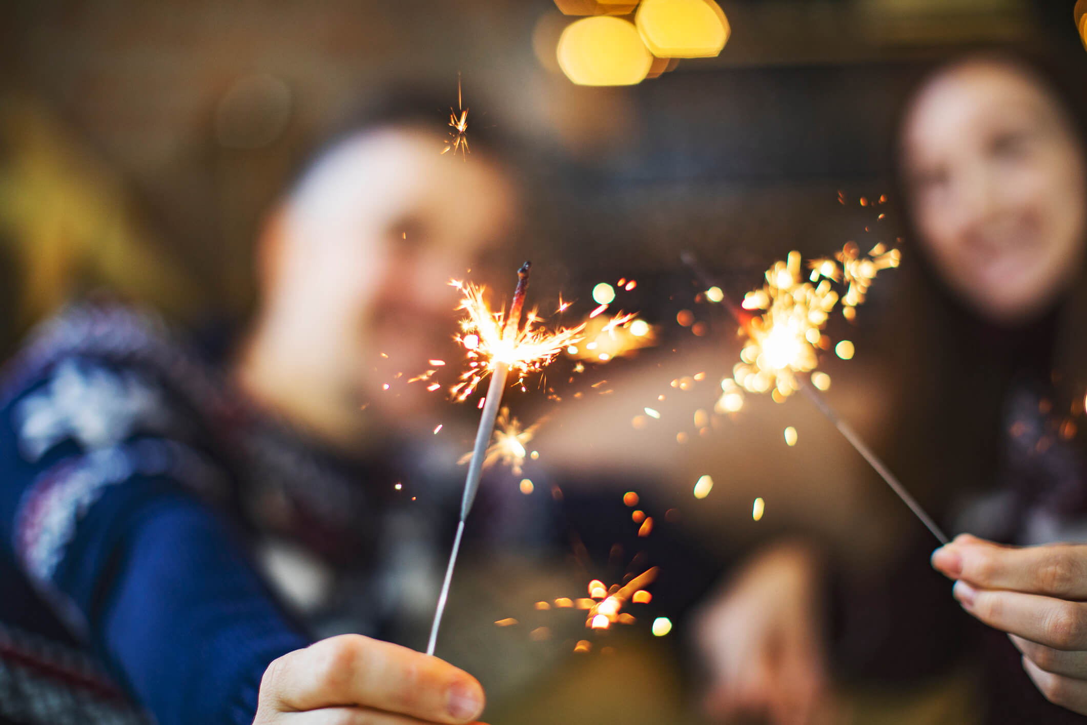 A couple wearing holiday sweaters holding sparklers in front of them